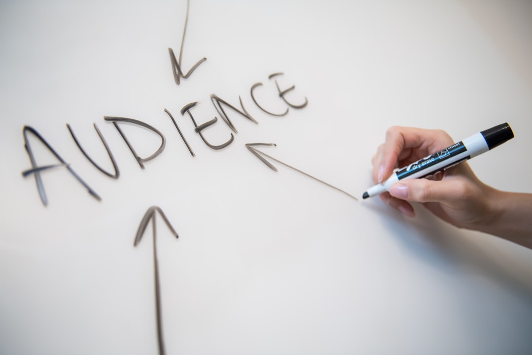 A woman’s hand writing the word audience on a whiteboard, with arrows.